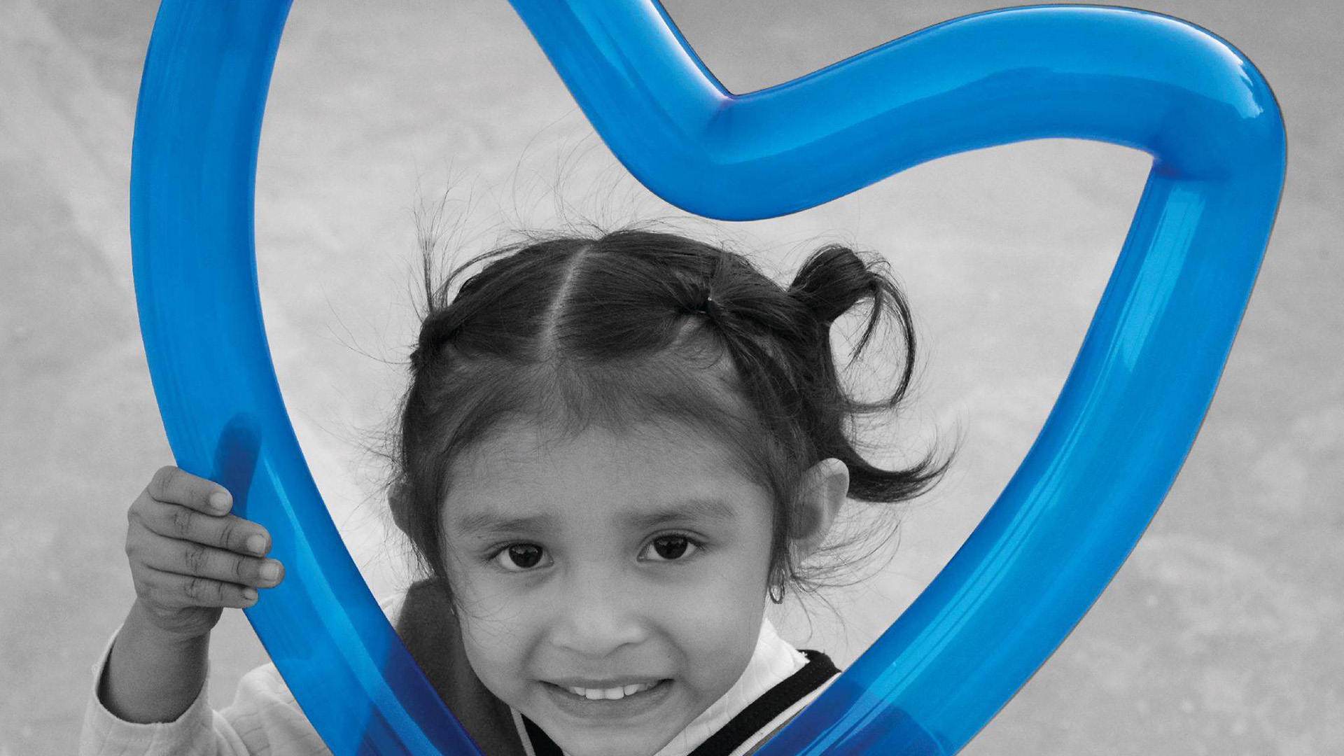 A young hispanic girl smiling through a blue balloon shaped like a heart